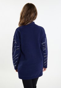 Marineblauer Langarm-Cardigan mit hohem Ausschnitt, der mit metallischen Fadendesigns an den Ärmeln und einem strukturierten Strickstoff versehen ist.