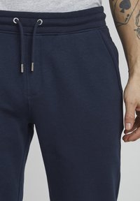 Navyblaue Jogginghose aus weichem Stoff mit einem elastischen Bund und Kordeln mit Metallspitzen, die ein lässiges Design und Seitentaschen zeigen.
