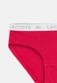 Κόκκινες βαμβακερές εσώρουχα με μαλακή υφή και ελαστική ζώνη μέσης, που φέρει το λογότυπο "LACOSTE" σε ανοιχτό γκρι. Καθαρές άκρες και εφαρμοστ�ή σχεδίαση.