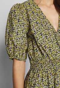 Květinové šaty s krátkými nabíranými rukávy a hlubokým výstřihem do V. Mají černé pozadí s bílými a žlutými květinami. S nabíraným pasem.