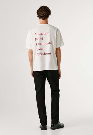 Weißes Baumwoll-T-Shirt mit rotem Text: „Authentic, Rebel, Unstoppable, Iconic, Pepe Jeans.“ Kombiniert mit schwarzen Hosen und Schuhen.