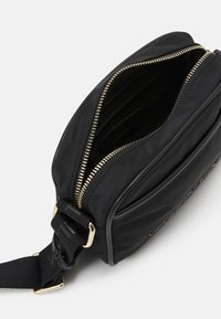 Svart syntetisk axelväska med guldfärgad dragkedja, har en strukturerad form och flera interna fack för organisering.