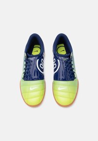 Par nogometnih cipela za zatvorene prostore u plavoj i žutoj boji marke Nike s vezicama i gumenim potplatom, prikazane odozgo na bijeloj pozadini.