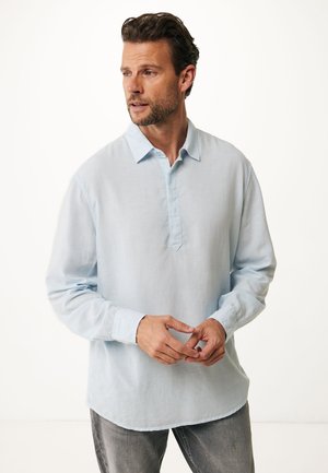 Camisa de manga larga de color azul claro hecha de una tela ligera, con una tapeta de botones y un dobladillo curvado, combinada con jeans grises.