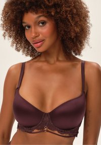 Biustonosz z koronkowym wykończeniem w ciemnym burgundzie, wykonany z gładkiego materiału, z drucikami wspierającymi, regulowanymi ramiączkami oraz dekoracyjnym akcentem na środku.
