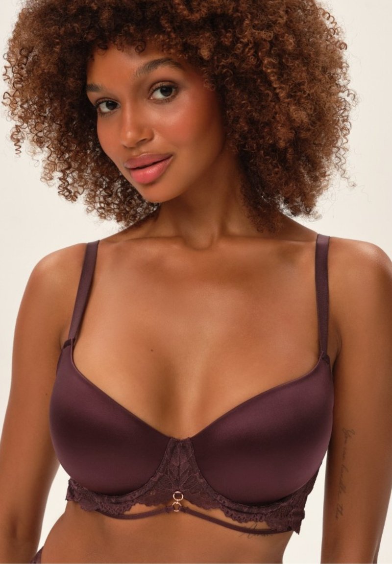 Biustonosz z koronkowym wykończeniem w ciemnym burgundzie, wykonany z gładkiego materiału, z drucikami wspierającymi, regulowanymi ramiączkami oraz dekoracyjnym akcentem na środku.