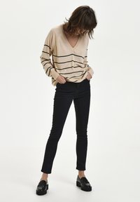 Pull beige à rayures noires horizontales, col en V, coupe décontractée, associé à un jean skinny noir et des mocassins noirs épais.