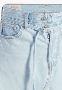 Jeans in denim azzurro chiaro presentano una vita alta, chiusura con bottoni, un leggero effetto sfumato e cuciture arancioni a contrasto, con un dettaglio di legatura sulla vita.
