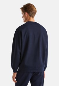 Námořnická modrá mikina vyrobená z měkkého materiálu, s uvolněným střihem, kulatým výstřihem a žebrovanými manžetami. Detaily zahrnují hladkou texturu a jemné švy.