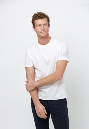 White short-sleeve t-shirt made of cotton, featuring a round neckline and smooth texture, paired with dark pants. Minimalist design.