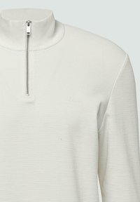 Witte half-zip pullover met een geribbelde structuur. Heeft een opstaande kraag en een klein logo op de borst. De rits heeft een metallic afwerking.