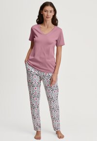Roze top met korte mouwen en V-hals, gecombineerd met witte broek met een bloemenpatroon in roze, blauw en groen. Zacht, lichtgewicht katoen.