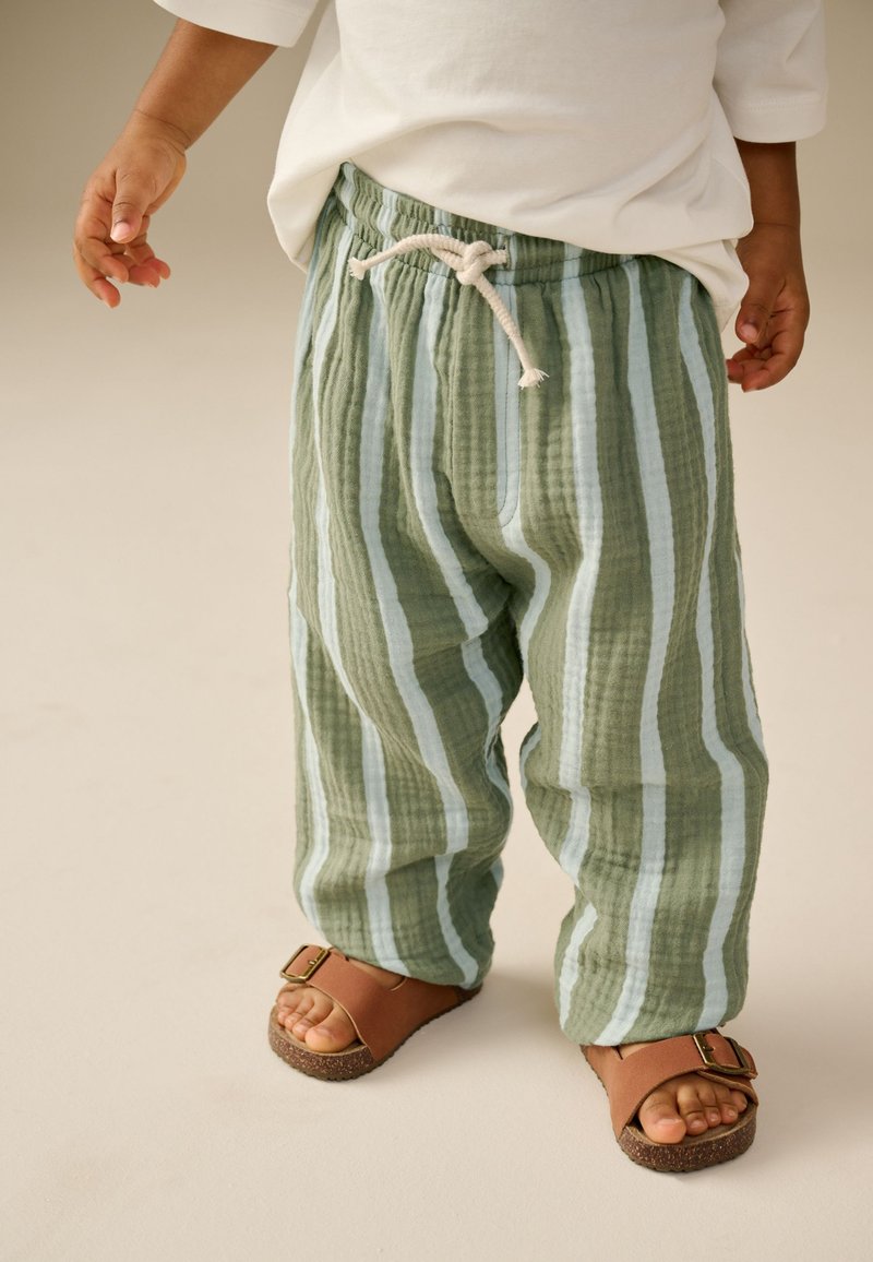 Pantalones holgados con rayas verdes y azul claro, de tela texturizada y cintura con cordón, combinados con sandalias marrones y pies descalzos.