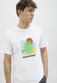 Camiseta de algodón blanca con un gráfico colorido de una planta de agave, un sol rojo y el texto "JACK&JONES" en negrita negra. Mangas cortas.
