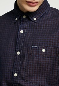 Camicia a quadri blu navy realizzata in tessuto testurizzato, con colletto button-down, bottoni bianchi e un piccolo logo G-Star sulla tasca.