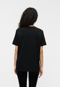 Μαύρο βαμβακερό t-shirt με κοντά μαν ίκια και στρογγυλή λαιμόκοψη, με άνετη εφαρμογή και λεία υφή. Η πίσω όψη δεν έχει λογότυπα ή σχέδια.