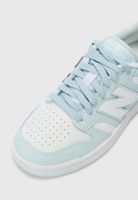 Baskets bleu clair avec un embout en cuir blanc perforé, lacets tissés et un côté texturé avec un détail de logo proéminent.