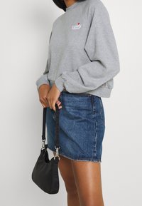 Sweatshirt gris avec le logo Levi's, associé à une mini-jupe en denim bleu et un sac à bandoulière noir. Présente une coupe décontractée et des poignets côtelés.