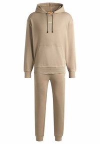 Beige hoodie and matching sweatpants set. Hoodie features a front pocket, drawstrings, and logo. Pants have cuffs at the ankles and a logo detail.