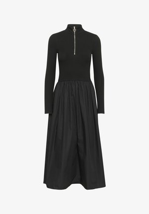 Fekete ruha bordázott, testhezálló felsőrésszel és magas gallérral. Ezüst cipzárral és laza, folydogáló szoknyával rendelkezik. Hosszú ujjú, egyszínű.