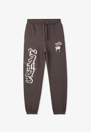 Pantaloni grigi in felpa con elastico in vita, caratterizzati da disegni in stile graffiti bianchi sui lati e gamba affusolata. Materiale misto cotone.