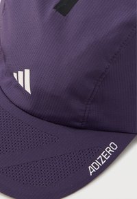 Μωβ αθλητικό καπέλο φτιαγμένο από υφασμάτινη υφή, με πάνελ από δίχτυ και λευκό λογότυπο με λεπτομέρειες. Δομημένη γείσο για προστασία από τον ήλιο.