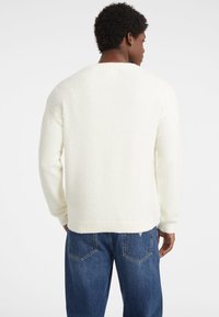 Witte, fluffy pull met een ronde hals en geribbelde manchetten, gecombineerd met blauwe jeans, getoond vanaf de achterkant.