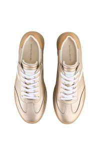 Beige sneakers with a smooth leather upper, white laces, and a gum rubber sole. Features include stitching accents and a logo on the insole.