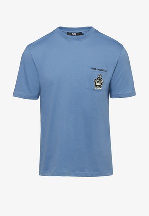 Jasnoniebieska koszulka z krótkim rękawem i kieszonką na piersi, na której znajduje się lampart w okularach przeciwsłonecznych oraz napis „KARL LAGERFELD” nad nim.