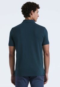 Dunkelblaues Poloshirt für Herren, kurze Ärmel, klassischer Kragen, schlanker Schnitt mit seitlichen Schlitzen, glatte Textur und minimale Nähdetails.