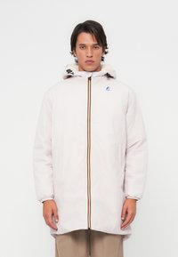 Parka rose clair avec capuche ajustable, fermeture éclair avant avec une bande de couleur, poignets élastiques et un petit logo sur la poitrine.