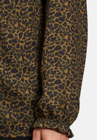 Tessuto con stampa leopardata con macchie nere su uno sfondo marrone; presenta dettagli con volant sui polsini, peso medio e texture liscia.