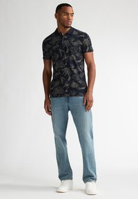 Marineblå polo-shirt med guldblomstermønster, korte ærmer og krave. Kombineret med lyseblå jeans og hvide sneakers.