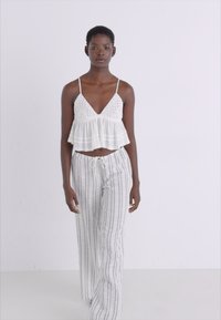 Haut blanc court avec des détails en dentelle, associé à un pantalon large à rayures claires doté d'une taille élastique et d'un cordon de serrage.