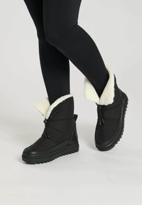 Zwarte enkellaarzen met een gestructureerd oppervlakte, uitgerust met een witte nepbont manchet, een duurzame rubberen zool en een verstelbare trekkoordsluiting.