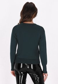 Pulover de culoare verde închis, cu tiv și manșete cu nervuri. Are accesorii din perlă pe umeri. Textură netedă, mâneci lungi și decolteu rotund.
