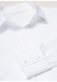 Camicia bianca con colletto classico, maniche lunghe e bottoni bianchi rotondi sui polsini, realizzata in un tessuto liscio.