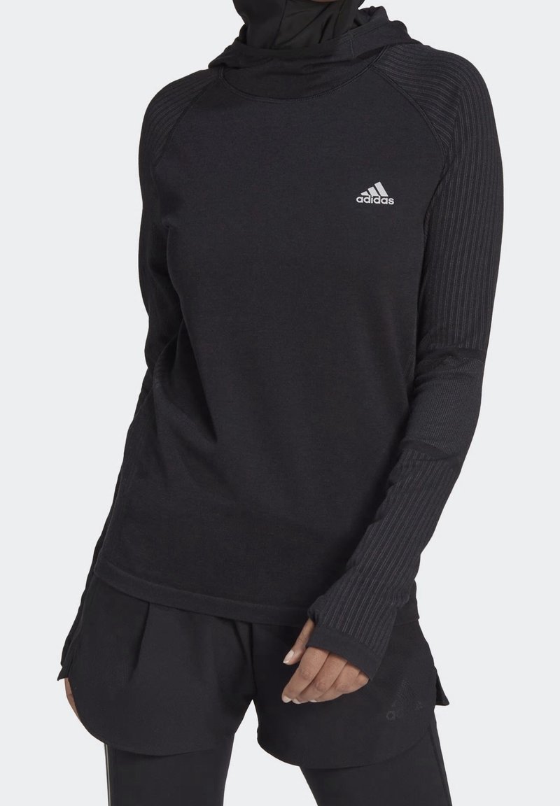 Haut de sport noir à capuche avec des accents côtelés sur les manches, arborant un petit logo Adidas blanc sur la poitrine et des passe-pouces aux poignets.