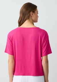 T-shirt a maniche corte e collo rotondo di colore rosa brillante, realizzato in tessuto morbido. Presenta una vestibilità rilassata e un orlo dritto sul retro.