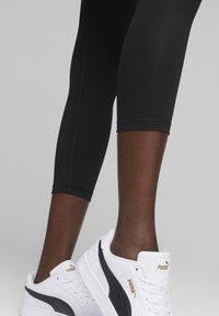Czarne legginsy sportowe bezszwowe w połączeniu z białymi i czarnymi sneakersami Puma z gładkiej skóry z złotymi akcentami.