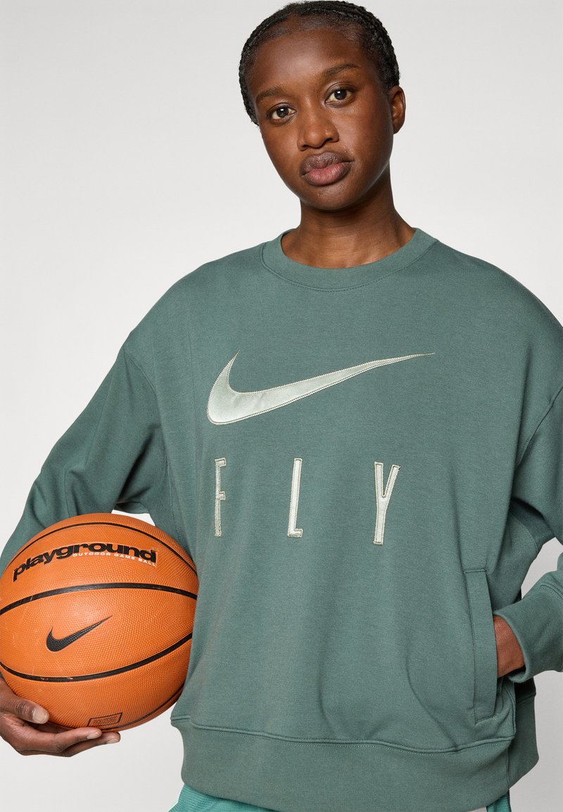 Felpa verde con un grande logo Nike argentato e il testo "FLY". Il modello tiene un pallone da basket arancione con il marchio "playground".