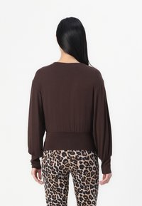 Brun langermet topp med en tettsittende midje, parret med leopardmønstrede leggings med svarte og brune flekker. Glatt stoff, avslappet passform.