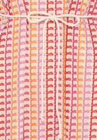 Gros plan d'un tissu en crochet multicolore avec des rangées verticales en rose, orange, rouge et violet, noué avec un nœud de corde blanc au centre.