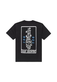 Camiseta negra con un gráfico en blanco y azul de una mano con enredaderas y flores, enmarcado con el texto "SIGUE CRECIENDO" en la parte inferior.