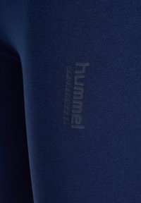 Close-up van donkerblauwe stof met subtiel verticaal bedrukt "Hummel Sportswear" logo op het materiaal.