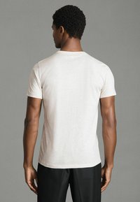 Tricou scurt cu mânecă scurtă, de culoare bej deschis, cu guler rotund, fabricat dintr-un material moale și respirabil, având o textură netedă și un design simplu.