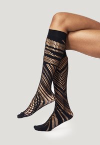 Calze nere al ginocchio con design a rete aperta e motivi geometrici, e una zona della punta solida. Materiale morbido con una texture liscia.