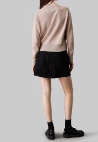 Beżowy sweter dziany z prążkowanymi mankietami, w połączeniu z czarną spódnicą dżinsową z tylnymi kieszeniami. Czarne buty dopełniają całość.