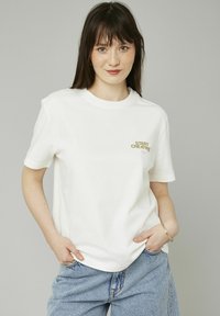 T-shirt en coton blanc à manches courtes et encolure ronde, avec l'inscription "START CREATING" imprimée en or et rose sur la poitrine.