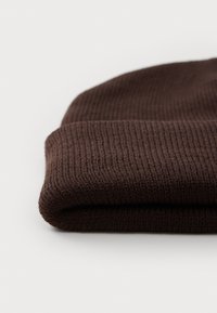 Berretto in maglia marrone con una texture a coste, caratterizzato da un design con risvolto e tessuto morbido, ripiegato e posizionato su uno sfondo bianco.